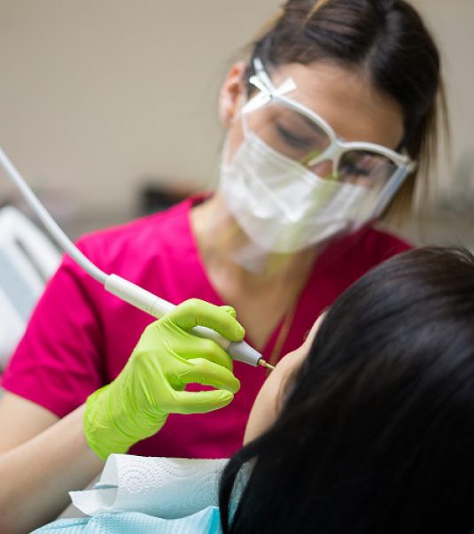 Female dentist cleaning teeth of a beautiful patient woman in dental clinic